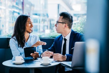 Modern çok ırklı kadın ve erkek kafeteryada kahve fincanları ve zımbırtılarla oturuyor ve iş projesi hakkında tartışıyorlar.