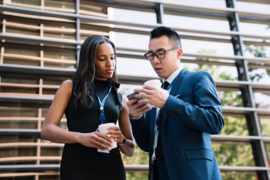 Molada kahve içen ve sokakta cep telefonunu paylaşan çok kültürlü genç kadın ve erkeğin...