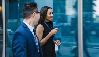 Afro-Amerikan kadın ve takım elbiseli adamın yan görünüşü. İsim etiketi takıyor ve boş zamanlarında sokakta yürürken konuşuyor.