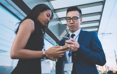 Şehir tren istasyonunda yan yana durup sohbet ederken cep telefonu kullanan, isim etiketli çağdaş kadın ve erkek.