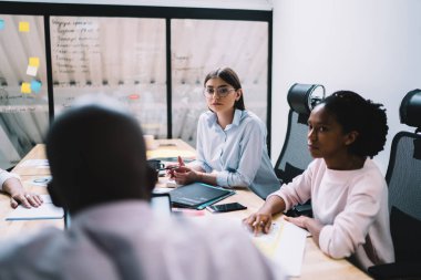 Masaüstünde oturan çok kültürlü erkek ve kadın tüccarlar finans direktöründen yeni iş stratejileri dinliyorlar. Konferans için zaman harcayan ciddi bir grup profesyonel iş arkadaşının arka planı.