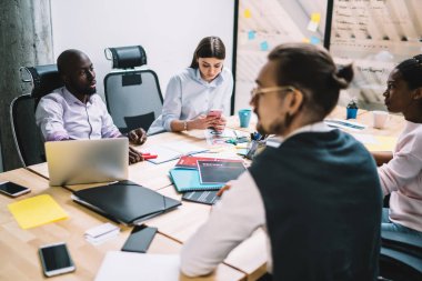 Proje üzerinde işbirliği yapmak amacıyla ofiste profesyonel iş arkadaşlarıyla birlikte otururken, akıllı telefon aygıtıyla posta yazan Kafkasyalı kadın yönetici