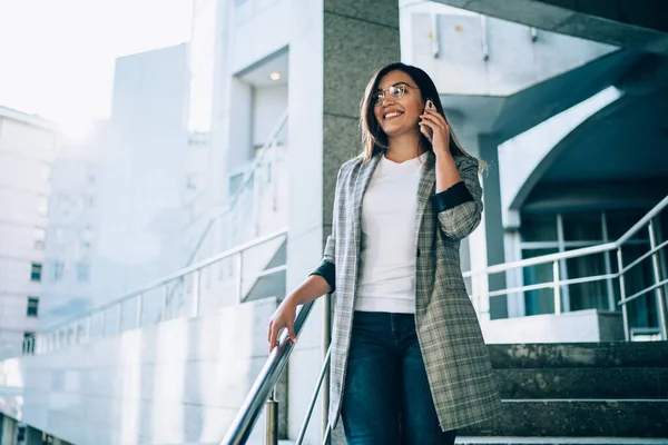 Turkish business woman in formal wear calling to colleague for discussing time of meeting on urban setting enjoying good roaming connection on smartphone device, concept of communication on phone