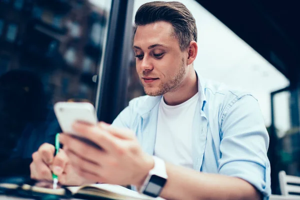 Nedenfra Holder Kjekk Mann Smarttelefon Mens Han Noterer Notisblokk Ved – stockfoto