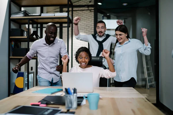 Excited diverse executive colleagues raising hands celebrating unbelievable online result, happy partners motivated by great achievement or team victory feeling amazed by received good news in email