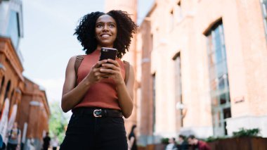 Sosyal ağlardan gelen takipçilerle çevrimiçi iletişim kuran ve gülümseyen pozitif hipster kız bakışlarının altında, modern teknolojiye sahip Afro-Amerikan genç kız