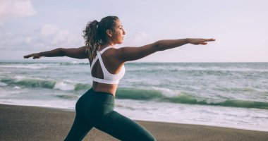 Moda eşofmanlı, enerjik, ince bir kadın sabahları yoga egzersizleri sırasında Warrior 1 yapıyor. Kadın jimnastik, doğayı canlandırmak için zaman ayırıyor. Farkındalık kavramı.