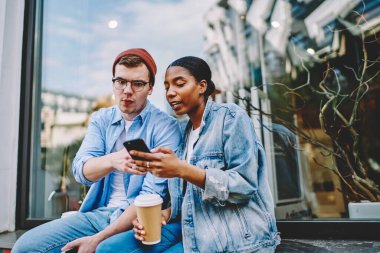 Akıllı telefondan uygulama gösteren Afrikalı Amerikalı genç bir kadın günlük kot giyen hippinin dışarıda kahveyle oturduğunu merak etti. Cep telefonundan video izleyen çok kültürlü arkadaşlar.