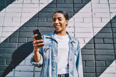 Akıllı telefon cihazında büyük satışları olan internet mağazasından bildiri alan neşeli Afro-Amerikan genç bayanın bakış açısının altında. Sosyal ağda cep telefonuyla pozitif koyu tenli sohbetler