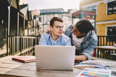 Değer veren Afrikalı Amerikalı hippi kız, modern dizüstü bilgisayarda uzaktan çalışan beyaz kocasını destekliyor. Netbook 'ta oturan erkek arkadaşı için endişelenen koyu tenli genç kadın.