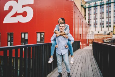 Gülümseyen beyaz bir adam, Afrika kökenli Amerikalı kız arkadaşını sırtında taşır. Şehre yerleşmiş, neşeli, romantik, çok kültürlü bir çift.