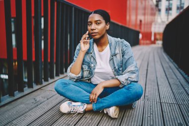 Kot ceketli Afrikalı Amerikalı bir kadın cep telefonuyla konuşurken kameraya bakıyor. Ciddi esmer tenli hippi kız şehir merkezinde cep telefonuyla konuşuyor.