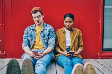 Birlikte dinlenen çok ırklı çift iletişimi görmezden gelip modern alet bağımlılığı ve ağ kurma üzerine yoğunlaşmış koyu tenli, kıskanç bir kadın erkek arkadaş akıllı telefonuna bakıyor.