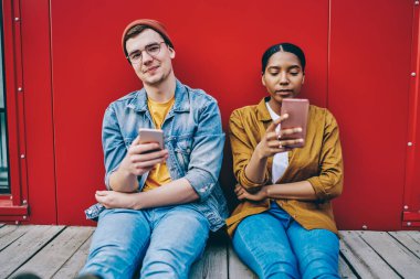 Yakışıklı beyaz erkek kameraya bakarken Afrikalı Amerikalı kız arkadaşı cep telefonuyla sohbet ediyor gerçek iletişimi görmezden geliyor, çok ırklı çift modern cep telefonlarını kullanarak birlikte vakit geçiriyor.
