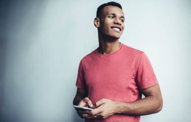 Neşeli koyu tenli, rahat giyinen, bakışlarını kaçıran ve gülümseyerek akıllı telefon cihazında takipçilerle sohbet eden, pozitif erkek blogcu dijital telefon ile zaman geçirmekten zevk alan mutlu bir adam.