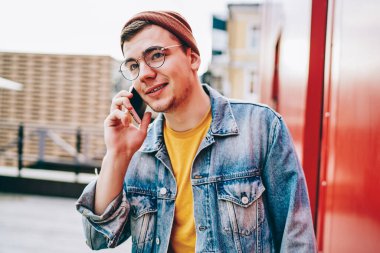 Giyim kuşamında ve gözlüklü genç yakışıklı hippi, gümrük vergileri hakkında operatörle cep telefonu kullanıyor, Kafkas asıllı bir erkek, gezici bir arkadaşla akıllı telefon görüşmesi yapıyor.