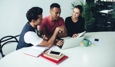 Başarılı okul öğrencileri, birlikte öğrenme konusunda beyin fırtınası toplantısında birbirlerine danışmanlık yapıyorlar. Masaüstünde modern dizüstü bilgisayarla çalışan erkek ve kadın öğrenciler.