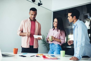 İş kurma projesinde işbirliği yaparken dokunmatik veri bilgilerini kullanan başarılı genç çalışanlar, ofis masaüstü bilgisayarının yanındaki canlı iletişim sırasında gülümseyen olumlu erkek ve kadın