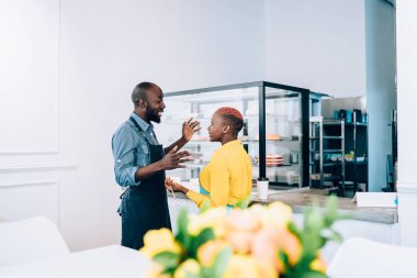 Afro-Amerikalı kadın ve erkeğin yan görüntüsü gülümsüyor ve restoranda birbirleriyle sohbet ederken hoş sohbetler ediyorlar.