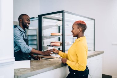Yakışıklı, Afro-Amerikan bir adamın gülümsemesi ve kahve evinde çalışırken çekici siyahi bir kadına sıcak içecek vermesi.