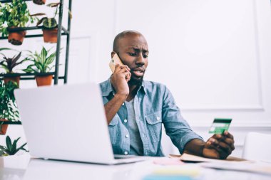 Kafe masasında oturup çalışırken günlük kıyafetli Afrikalı bir adam telefonla konuşuyor ve kredi kartı numarasını okuyor.