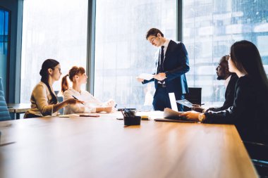 Bir grup genç çoklu etnik gruptan insan güneşli bir ofiste masada oturuyor ve genç yöneticiler işlerini kontrol ediyorlar. 