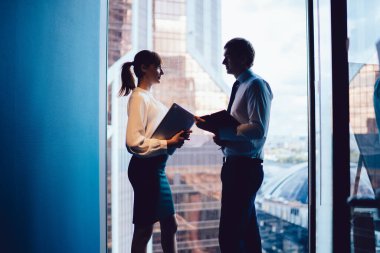 Ofiste şehir manzaralı pencereye karşı tartışırken, çağdaş zarif kadın ve adamın elinde belge dosyaları tutarken yan görünümü