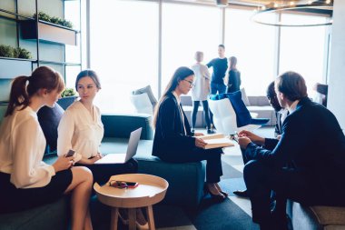Modern resmi çeşitlilikte kadın ve erkek grupları ofis salonunda toplanıyor. Gün ışığında iletişim kurarken belgeler ve cihazlarla çalışıyorlar. 