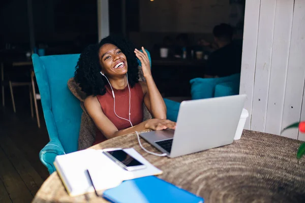 興奮したアフリカ系アメリカ人の女子学生は オーディオブックで受信した情報から良い感じのヘッドフォンで 明るい女性はカフェテリアで近代的な技術を使用している間に肯定的な音楽を聞いて — ストック写真