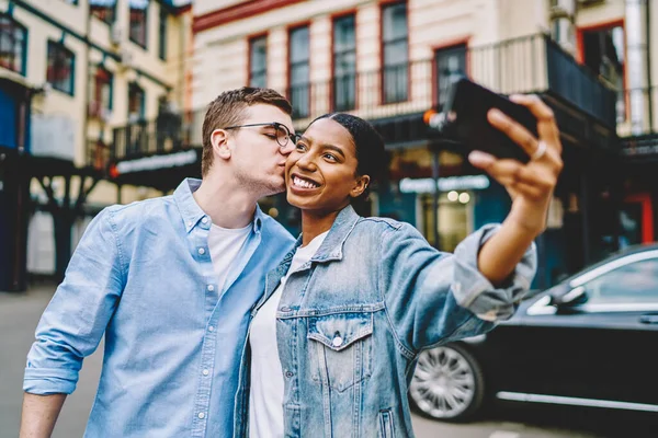白人嬉皮士亲吻快乐的非洲裔美国女友 她在城市旅行时手持智能手机 自私自利 — 图库照片