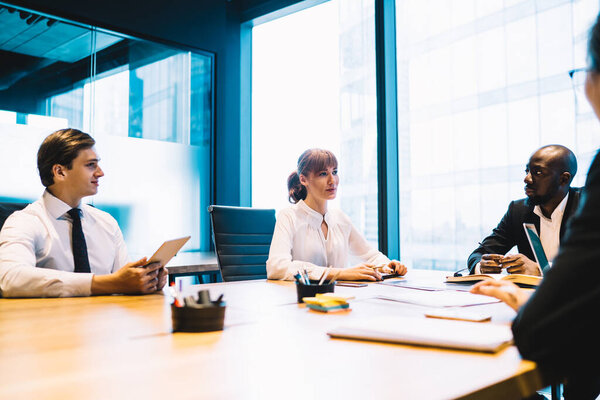 Group of multiracial professional business people sitting at table in light boardroom gathering on business conference to discuss idea of new project 