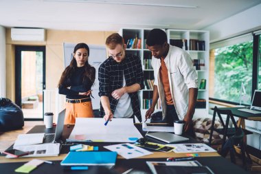 Çağdaş ofiste masa başında duran kağıt üzerine plan çizerken, modern kadın ve erkekler stratejilerini tartışıyor. 