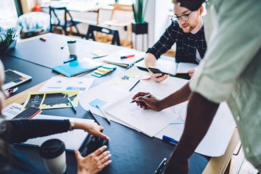Çok ırklı kadın ve erkeklerden oluşan bir grup masa başında yeni projenin kağıt çizim planıyla ve ekip halinde tartışarak