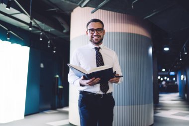 Şirket ofisinde iyi hissetmeyi planlayan neşeli muhasebecinin yarım boy portresi, çalışma alanında kameraya gülümseyen gözler için optik gözlük takan neşeli adam.