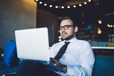 Vizyon düzeltmesi için gözlüklü yakışıklı erkek tüccar netbook üzerinden ofis kablosuna bağlı finans sitesinde bilgileri kontrol ediyor, beyaz tişörtlü beyaz adam dizüstü bilgisayarla veri arıyor