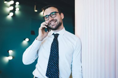 Gözlüklü, gülümseyen, modern cep telefonuyla iletişim uygulamasını kullanan mutlu bir adam akıllı telefon aygıtıyla iletişim kurmak için meslektaşını arıyor.