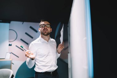 Toplantı odasında sunum yapmak için çalışırken kameraya bakan hayret içindeki işadamının yarı boy portresi, göz koruması için optik gözlük takan harika erkek simsar.