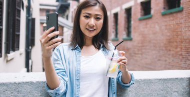 Çekici gülümseyen kadın turistin yarım boy portresi, cep telefonu uygulaması ve teknoloji konseptiyle çevrimiçi video çekerken elinde su içeceği ve kameraya gülümsüyor.