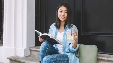 Su içeceği ile pozitif kadın okuyucunun portresi ve şehir ortamında dinlenen ilginç çok satanlar ve boş zamanlardaki kameralara gülümseme, gençlik yaşam tarzı ve hobi zamanı konsepti