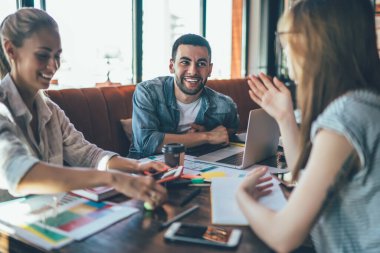 Modern kafede dizüstü bilgisayarı ve not defteriyle oturmuş mutlu bir şekilde sohbet eden bir grup çağdaş kadın ve erkek.