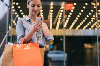 Alışveriş çantalı, modaya uygun hippi kız satış mağazalarında fiyatları kontrol etmek için akıllı telefon aygıtı kullanıyor. Reklam alanında 4G kablosuz bağlantıları var. Uygulama üzerinden mutlu beyaz kadın sohbeti.
