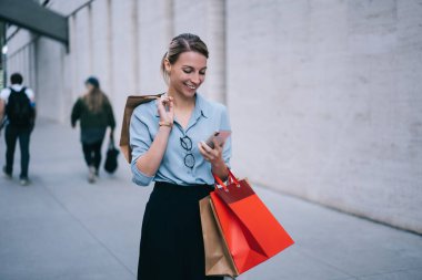 Modern uygulama üzerinden mesaj göndermek için akıllı telefon kullanan mutlu kadın, kişisel moda blogunda Kara Cuma satışları ile ilgili yayınları paketlerle paylaşan kadın müşteri