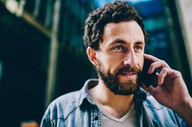 Şehir merkezinde sakallı ve akıllı telefon cihazıyla konuşan yakışıklı beyaz adam. Kot tişörtlü yakışıklı genç cep telefonundan arıyor ve gezici bağlantı kullanıyor.