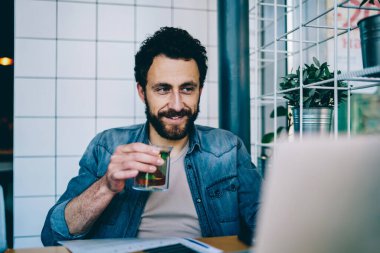 Kot giyip çay içen sakallı bir genç modern dizüstü bilgisayarda internetteki kablosuz interneti kullanarak ders seyrediyor. Kafkasyalı hippi Netbook 'ta moladan keyif alıyor.