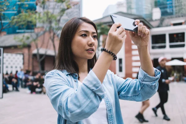 Asyalı kadın cep telefonuyla görüntülü şehir görüşünü alıp sokak ortamında dururken cep telefonuyla sohbet ediyor, kadın cep telefonu tutuyor ve kişisel turistik web günlüğü için resimlere tıklıyor