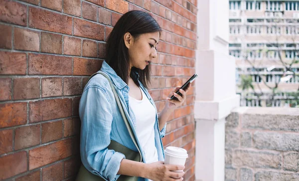 女性観光客とともにテイクアウトカップのカフェイン飲料検索情報ウェブサイト経由携帯電話 中国語ミレニアルヒップスター女の子読書テキストメッセージ上の携帯電話の支出時間都市部 — ストック写真