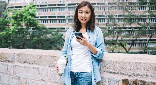 Sıradan giyinmiş, elinde hazır yemek kupası olan ve sosyal ağlara medya dosyalarının çevrimiçi paylaşımı için boş zamanlarında kameraya gülümseyen Çinli hippi kızın yarım boy portresi.