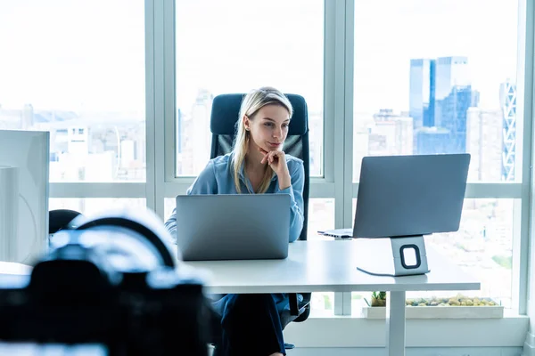 有重点的职业女性在办公室的办公桌前 靠着三脚架摄像机拍摄视频 一边看着笔记本电脑和电脑 — 图库照片