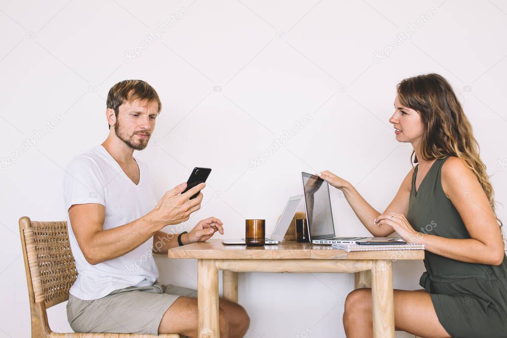 Serious male and female IT professionals communicating about brainstorming on project during distance job, young male checking schedule in smartphone organiser connecting to public internet