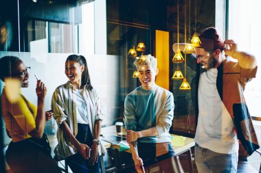 Neşeli milenyum kuşağı öğrencileri gündelik kıyafetleriyle birlikte projeden bahsederek eğleniyorlar. Çok ırklı erkek ve kadın meslektaşları ofisteki iletişim için gülüyorlar.